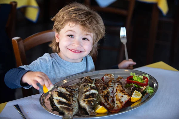 笑顔だ。子供のための健康的な食事。健康的な夕食のための魚のグリル。レストランで笑顔を見せる男の子. — ストック写真