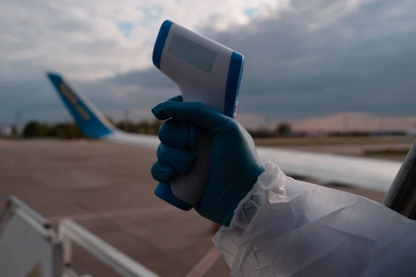 Covid. Measure body temperature at the border and aeroport. Steward in gloves holds a thermometer for measuring passengers temperature of the aircraft before flight. Covid 19 coronaviruse protection.