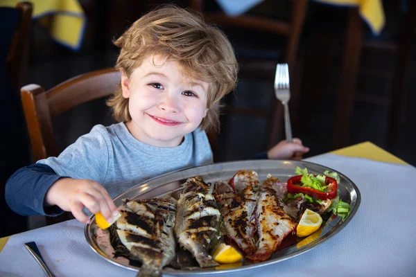 家庭でのレストラン食品。隔離中の調理。ロックダウン中の家庭での家族の夕食の伝統。その少年はテーブルで魚を食べる。海のディナー. — ストック写真