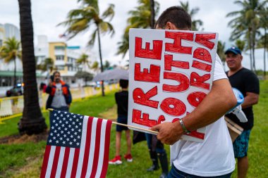 Miami Beach, Florida, ABD - 10 Mayıs 2020 Anti Coronavirus gösterisi. COVID-19 kısıtlamalarına karşı olan insanlar. Bedava Güney Florida tabelası ve Amerikan bayrağı. Kapanış plajlarını ve dükkanları protesto eden bir adam.