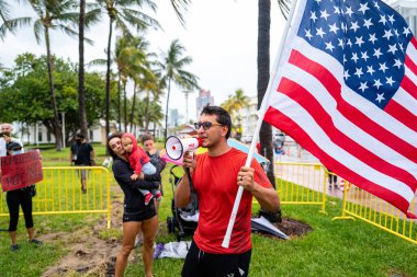 Miami Beach, Florida, ABD - 10 Mayıs 2020: Coronavirus gösterisi. Gösteride ailesi olan bir adam. Adam haklar hakkında hoparlöre bağırıyor. Protestocu, yüz maskesi takmanın anlamı olmadığını söyledi..