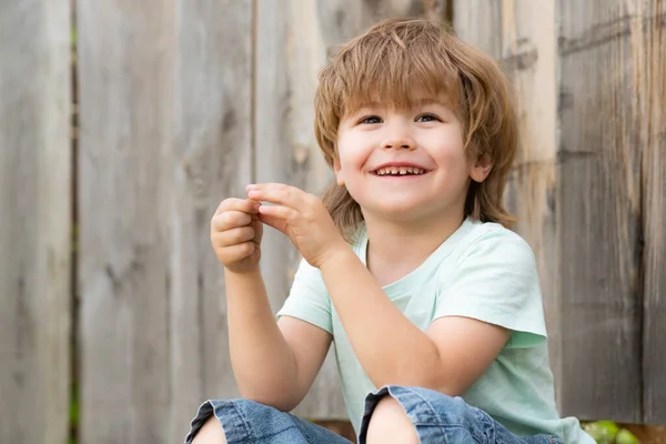 El niño feliz sonríe. Un niño se sienta en el jardín en el patio trasero . — Foto de Stock
