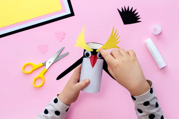 Making a penguin from colored paper and a roll of toilet paper. Children\'s art project. Step by step photo instruction. Step 7. Glue yellow details of the eyebrows.