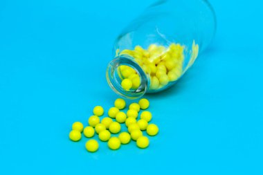 Cam kavanozdan dökülen sarı haplar. Mavi arkaplandaki ilaç kapsülleri.
