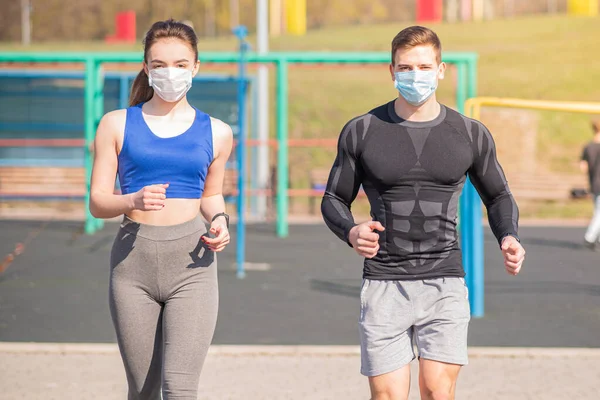 A young guy and a girl in medical masks run around on the playground during a pandemic. COVID-19. Health care.