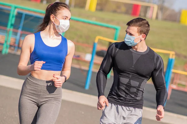 A young guy and a girl in medical masks run around on the playground during a pandemic. COVID-19. Health care.