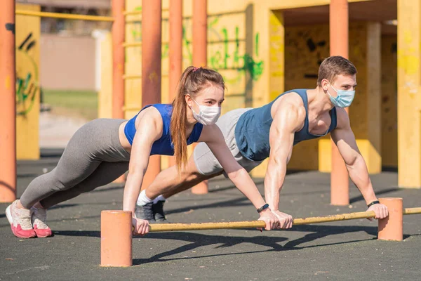 A sports guy and a girl in medical masks push up on the bar during a pandemic. COVID-19. Health care.