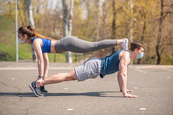 A sports guy and a girl in medical masks are push up during a pandemic. COVID-19. Health care.