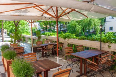 Nehir kenarındaki terasta yeşil bitkilerle çerçevelenmiş şirin bir yaz restoranı..