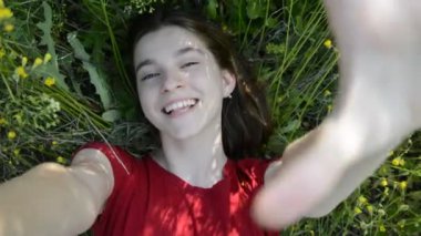 Mutlu genç kız, otların üzerinde uzanmış, tepeden manzaralı bir selfie çekiyor..