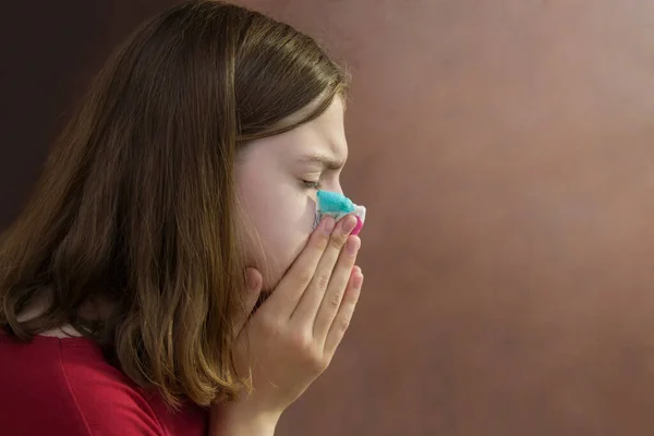 Sick young girl blows her nose in a napkin. Runny nose, headache, illness, allergy. Side view. Copyspace. — Stock Photo, Image