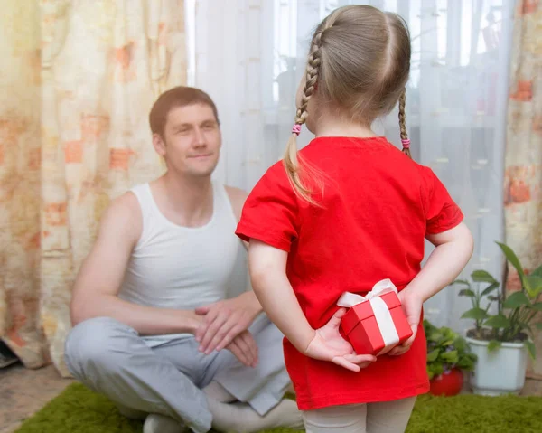 Hermosa niña rubia oculta un regalo a sus espaldas y quiere felicitar a papá en el día de su padre . —  Fotos de Stock