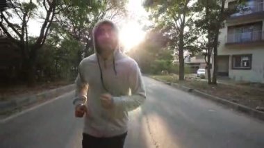 Yetişkin Asyalı bir adamın kapüşonlu tişört giyip şafak vakti koşarkenki fotoğrafı.