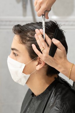 Covid-19 'un hapsi sırasında annesi saçını keserken koruyucu maskeli bir çocuğun yakın çekimi.