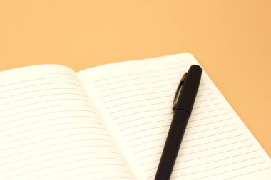 Turuncu arka planda siyah kalemli boş defter, iş planlama konsepti. Mesaj için yer var. Kapatın. Model