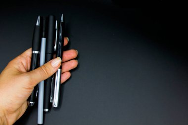 Kadın el ele tutuşuyor ve siyah arka planda izole edilmiş dört adet geleneksel siyah ve gri kalem gösteriyor. Metin için boşluk, kapat