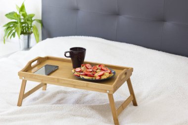 Kahvaltı tepsisi sağlıklı krepler, çilek, sıcak içecek ve beyaz arka planda yeşil bitki içeren bir yatağa kurulmuş. Sabah kahvaltısı konsepti. Mesaj için yer var. Model