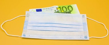 Tıbbi koruyucu cerrahi mavi maske, turuncu arka planda 100 Euro 'luk banknotların üzerinde yatıyor. Seçici odaklanma. Yüz maskeleri için fiyat artışı. Mesaj için yer var. Kapat..