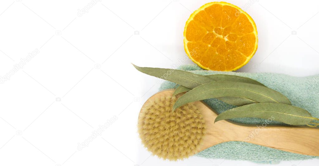 wooden eco natural brush for Dry body massage on towel near the green sprig of eucalyptus and orange on white background. anti cellulite treatments concept. Top view. Space for text