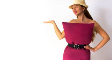 Kırmızı yastıklı ve yaz şapkalı ateşli bir kadın beyaz stüdyo arka planında gösteriler yapıyor. Moda kızı. Ev izolasyonundan dolayı yastık yarışması. Caronavirus Karantinası. Yaklaş. Metin için boşluk