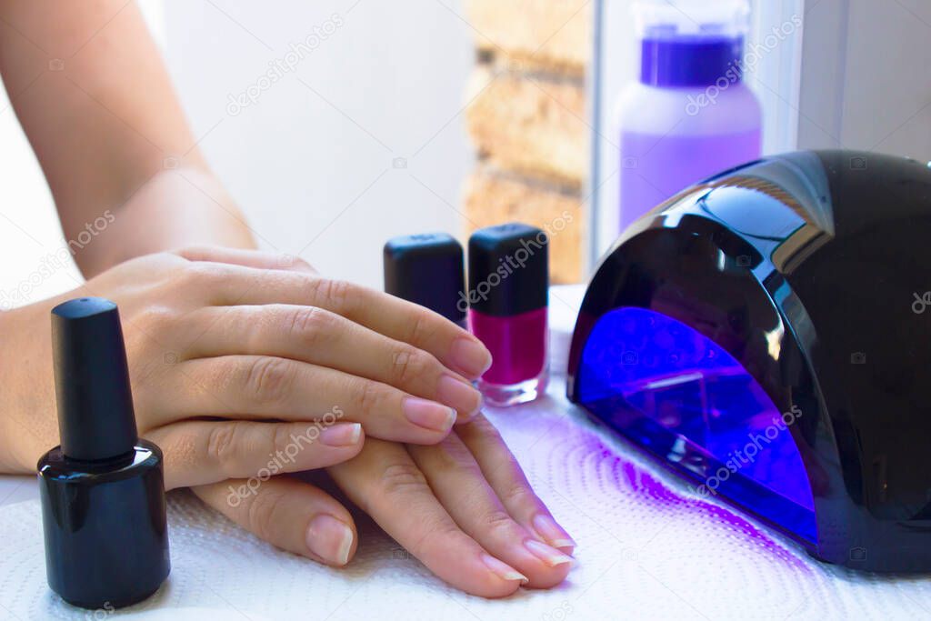 women hands near ultraviolet UV light LED lamp. close up. Nail lamp dryer for gel nail polish. home nail care