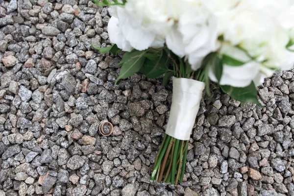 Brides rustic bouquet of white roses and golden rings on stones — Stock Photo, Image