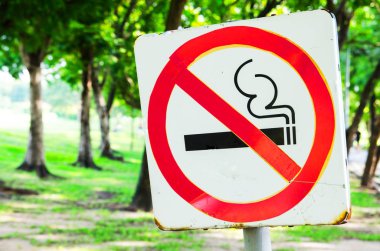 Parlak yeşil ağaçlar ve çim arka plan üzerinde parkta hiç Sigara İçilmez işareti.