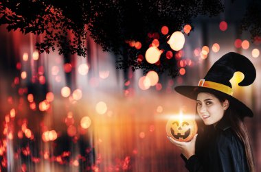 Büyülü bir balkabağı olan Cadılar Bayramı Cadısı, cadı şapkalı ve kostümlü güzel bir kadın.