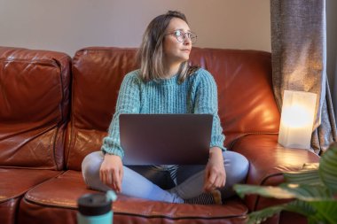 Evdeki kanepede laptopuyla çalışan genç bir kız.