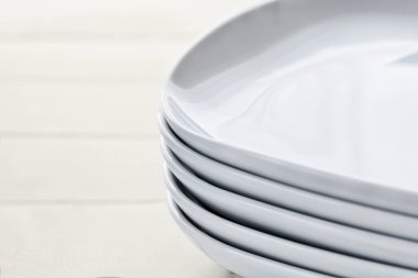 Tahta beyaz arka planda yuvarlak kenarları olan dikdörtgen beyaz seramik tabaklar yığını. Klasik porselen takımları parlak, temiz kaseler. Yığılmış kare plakalar. Kırsal tarzda. Uzayı kopyala, makro