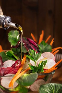Kırsal arka planda zeytinyağı soslu sebze salatası. Zeytinyağı akıntısı ve sağlıklı taze sebze salatası. Bir kase yeşilliğe zeytinyağı dökülüyor. Metin için alanı kopyala