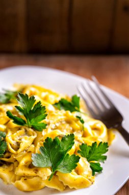 Tahta kırsal yüzeyde taze maydanoz yapraklı Ravioli. Geleneksel İtalyan mutfağı. Beton kahverengi masada kremalı sosun altında ravioli pişirilmiş makarna. Makro