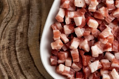 İtalyan pancetta, pastırma küpleri, doğranmış jambon, ahşap desenli yüzeyde kare beyaz tabakta kesilmiş domuz eti. Makarna için yemek malzemesi, geleneksel İtalyan yemeği. Üst manzara, kapat, makro.