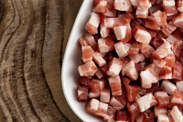 İtalyan pancetta, pastırma küpleri, doğranmış jambon, ahşap desenli yüzeyde kare beyaz tabakta kesilmiş domuz eti. Makarna için yemek malzemesi, geleneksel İtalyan yemeği. Üst manzara, kapat, makro.