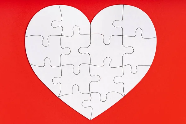 Jigsaw puzzle pieces in form of heart on red background. Love, charity, donation, helping concept. Perfect match, reunion.