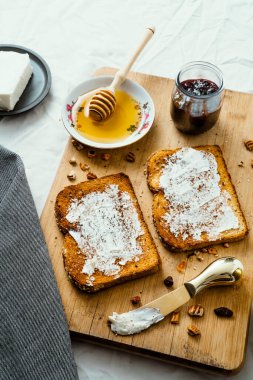 Ballı kızarmış ekmek, krem peynir ve kırmızı meyve reçeli, masa ve ahşap üzerinde.