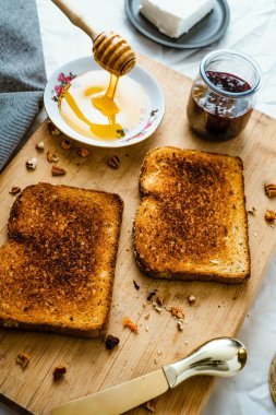 Ballı kızarmış ekmek, krem peynir ve kırmızı meyve reçeli, masa ve ahşap üzerinde.