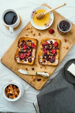 Ballı kızarmış ekmek, krem peynir, kırmızı meyve reçeli ve kahve, masa ve ahşap üzerinde.