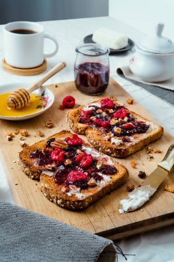 Ballı kızarmış ekmek, krem peynir, kırmızı meyve reçeli ve kahve, masa ve ahşap üzerinde.