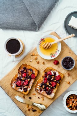 Ballı kızarmış ekmek, krem peynir, kırmızı meyve reçeli ve kahve, masa ve ahşap üzerinde.