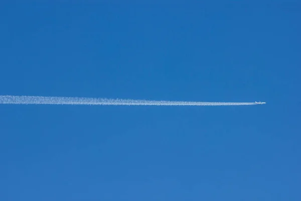 Derin mavi gökyüzünde uçan bir yolcu uçağı arkasında uzun beyaz bir jet akıntısı bırakıyor..