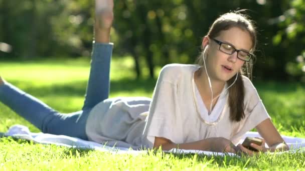 Ung kvinna Lyssna på musik och använda smartphone i parken — Stockvideo