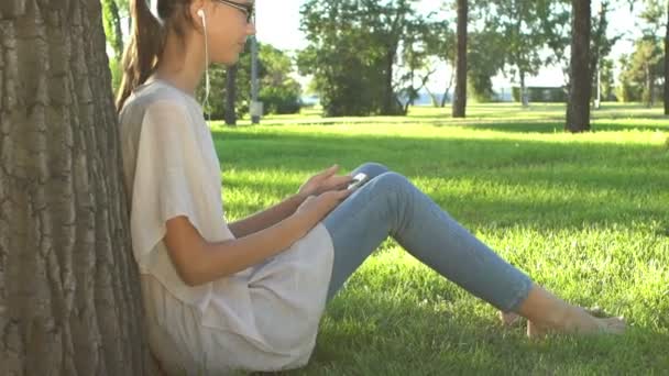 Νεαρή γυναίκα ακούγοντας μουσική και χρησιμοποιώντας το smartphone στο πάρκο — Αρχείο Βίντεο
