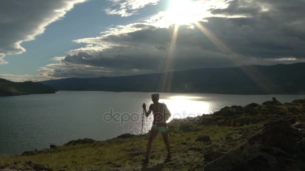 Νεαρή γυναίκα με σακίδιο πεζοπορία στα γύρω βουνά και τη λίμνη — Αρχείο Βίντεο