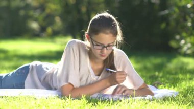 Genç güzel kız çayır üzerinde not defterine yazar