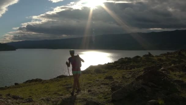 Νεαρή γυναίκα με σακίδιο πεζοπορία στα γύρω βουνά και τη λίμνη — Αρχείο Βίντεο
