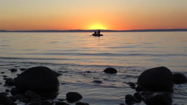 Silhouette of men in boat at sunset against bright golden sun and red sky — Stock Video