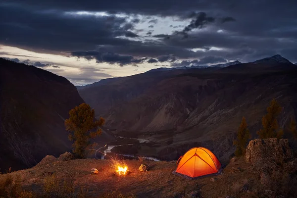 Una carpa iluminada y fogata en las montañas al amanecer — Foto de Stock