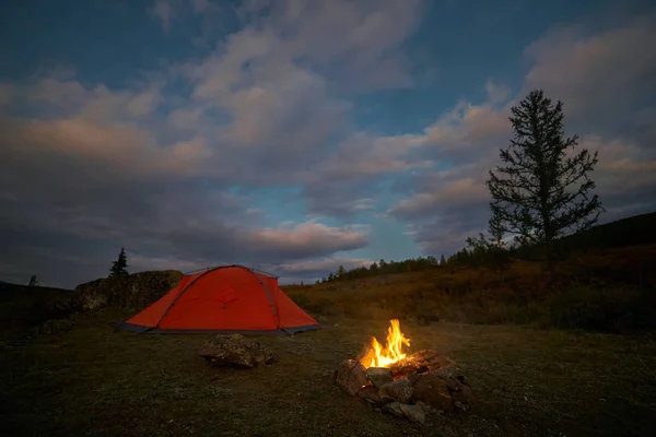 A tent and campfire under an evening sky