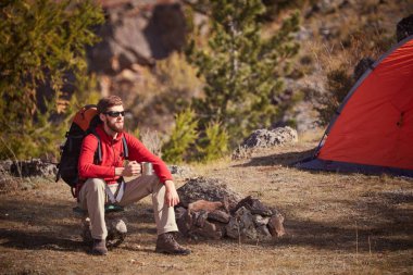 Backpacker dinlenme Kupası ile turuncu çadır yakın elinde olması.